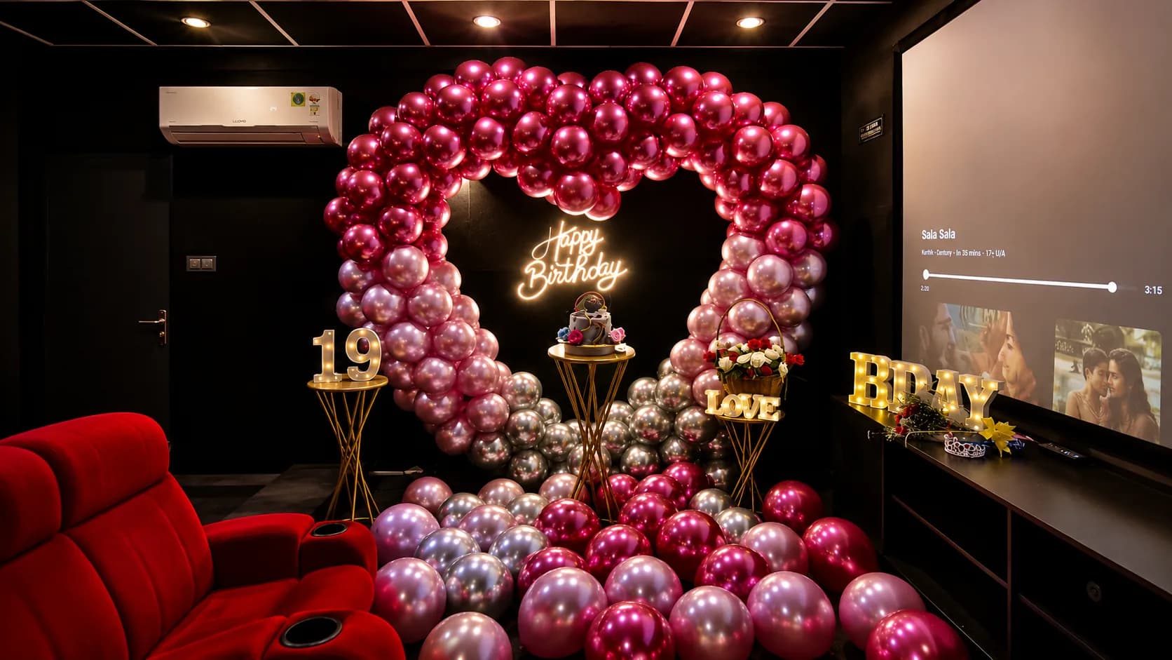 A magenta, pink and silver balloon heart around a neon Happy Birthday sign, with a cake on a gold stand, a rose basket and lit 19, LOVE and HBD letters