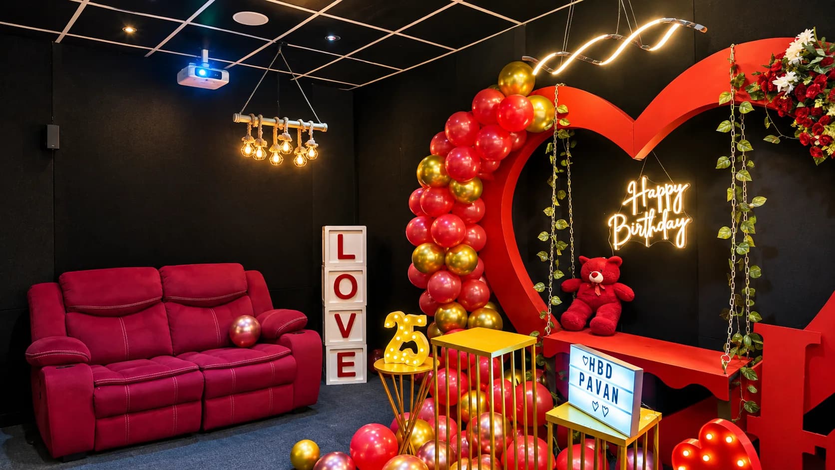 A magenta recliner sofa in a black room beside a red heart backdrop with a gold swing, a teddy bear and a neon Happy Birthday sign, under a ceiling projector and bulb lights