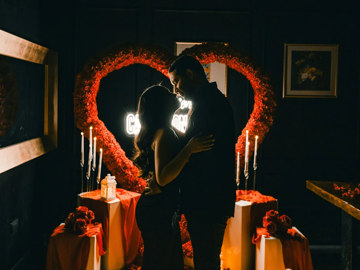 A couple standing together in front of a lit heart arch surrounded by candles