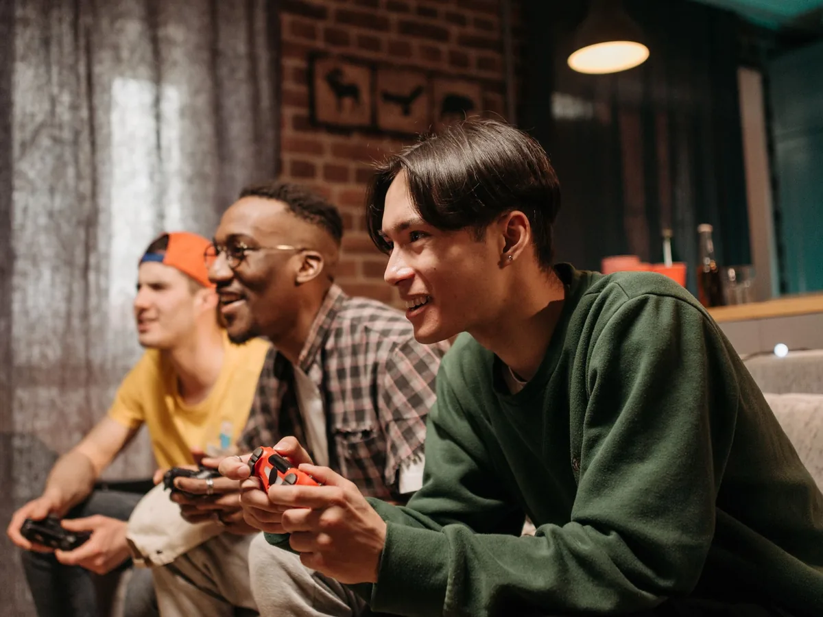 Three friends side by side on a sofa with game controllers in their hands
